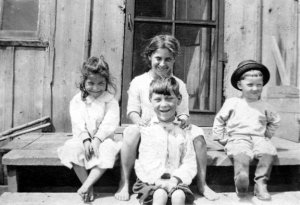 This photo, taken about 1920, illustrates the dillapidated condition of the farmhouse my grandparents moved to. Pictured are (L-R) my aunt, my mother, my Uncle Melvin, and Earl, whose body has not yet become as twisted as it would later in his life.